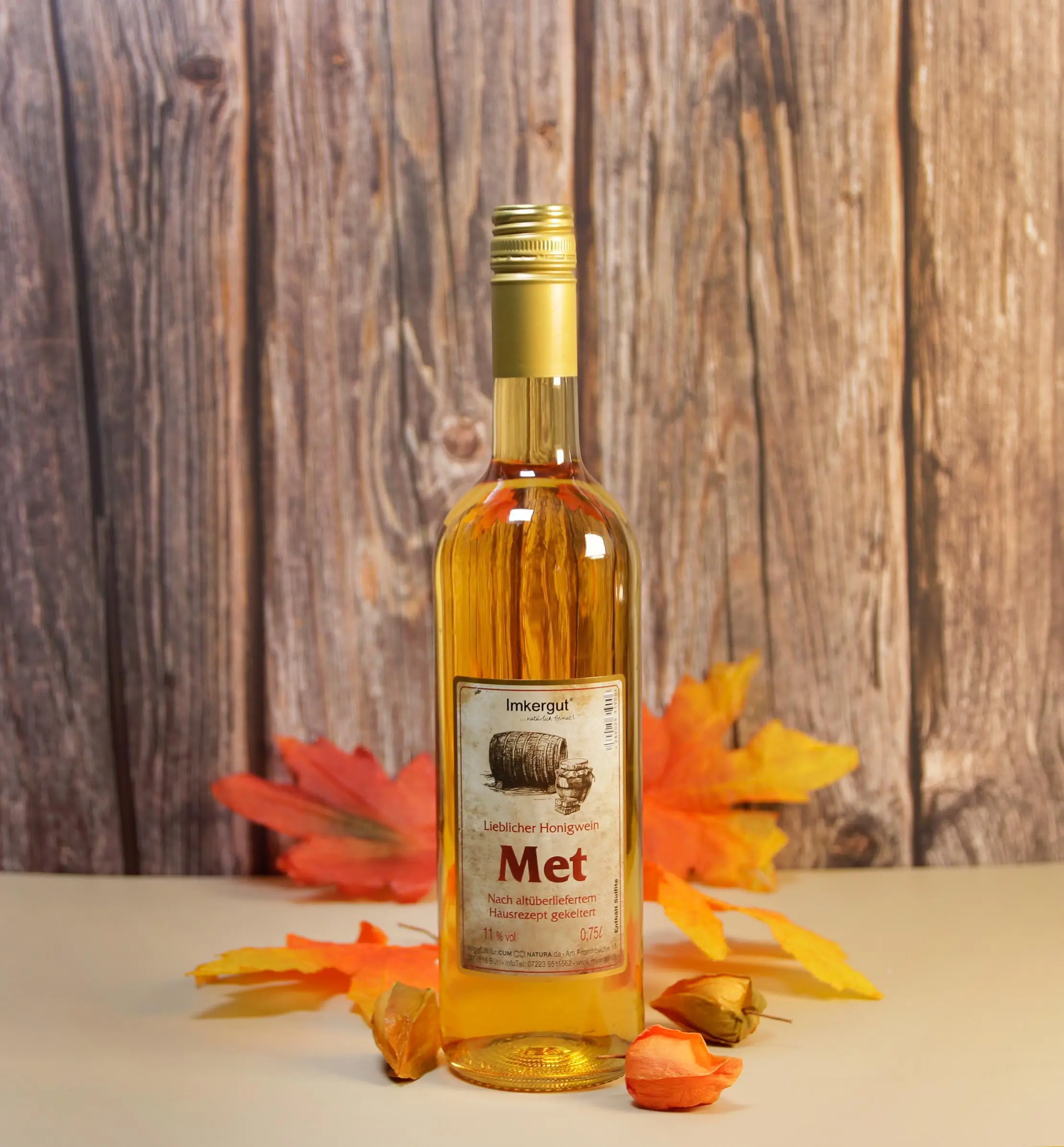 Eine Flasche Met vor einem Hintergrund aus Holz, drumherum herbstliche Blätter und Pflanzen